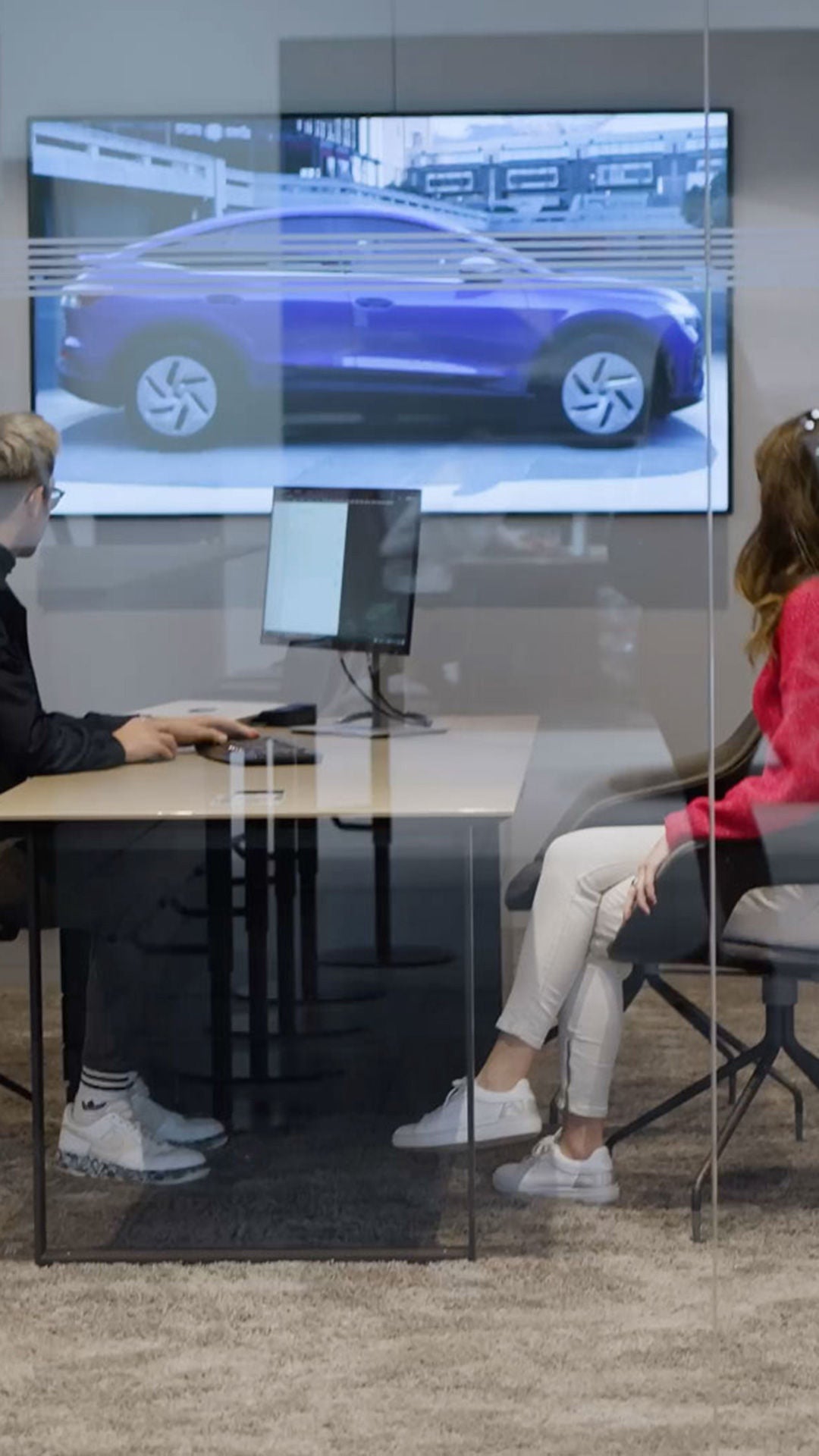 Zwei Menschen sitzen sich an einem Schreibtisch gegenüber und betrachten auf einem second Screen einen Audi.