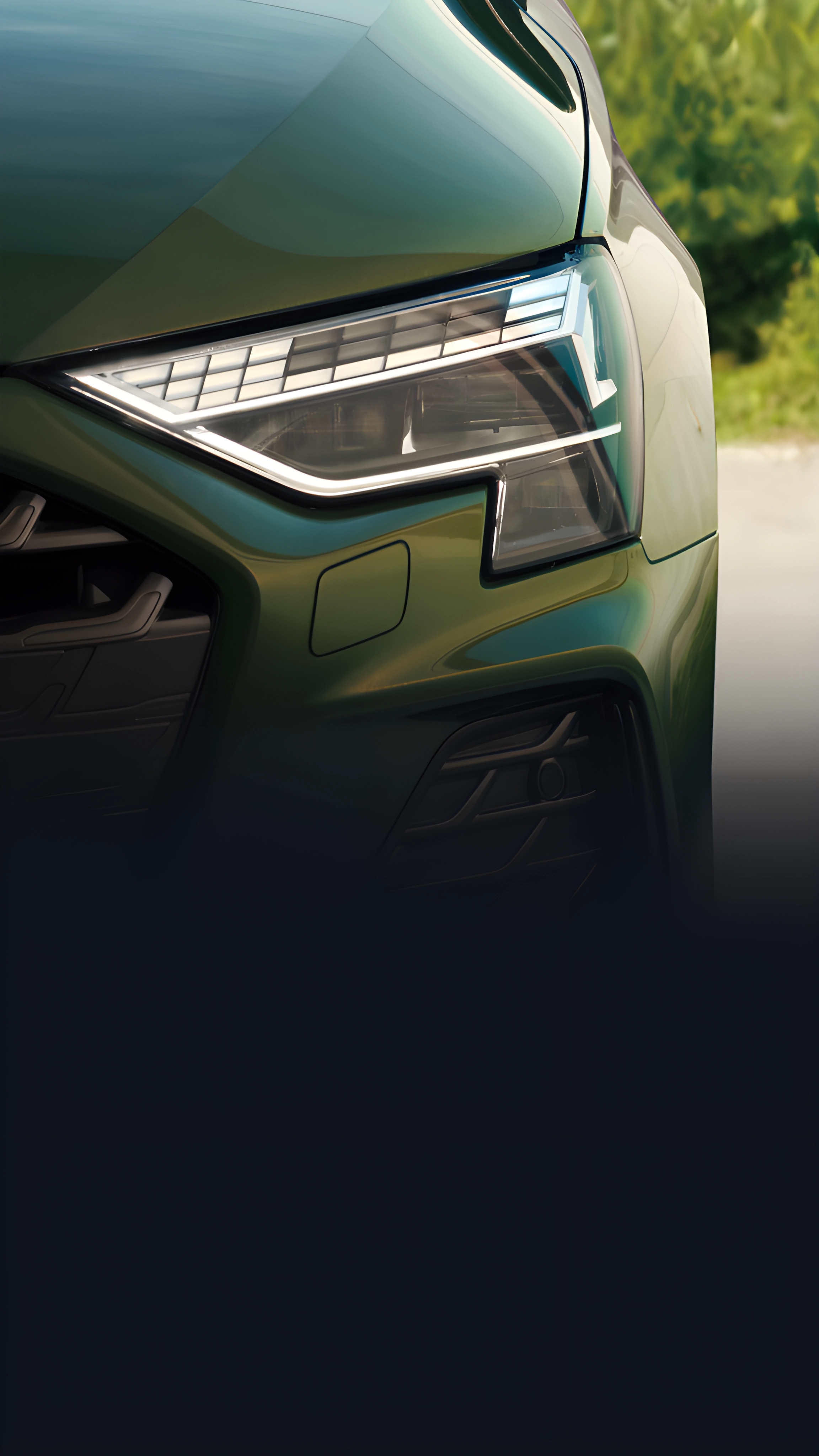 Green Audi A3 Sportback's front headlight and bonnet, with road and trees in background.