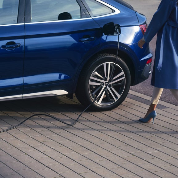 A person in a blue coat is plugging a charger into a blue electric car.