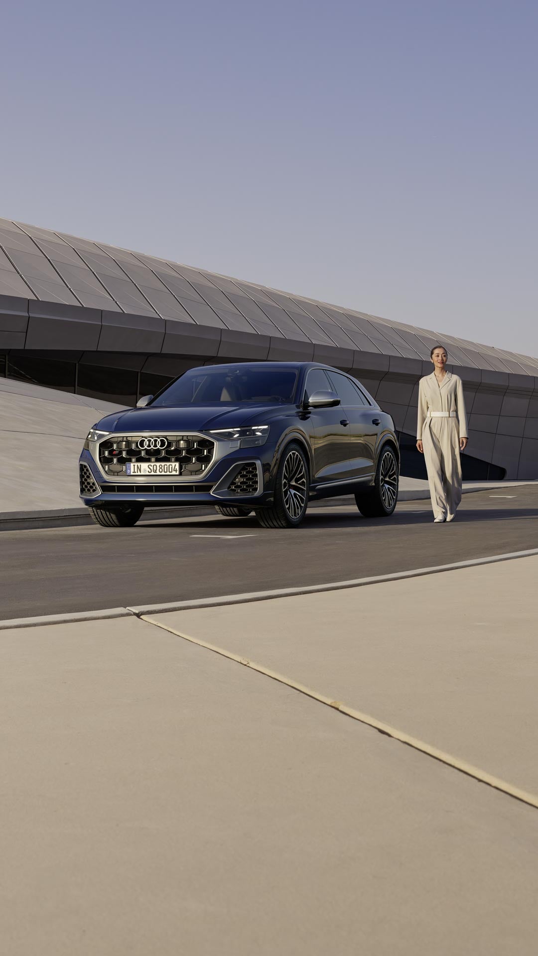 Eine Frau steht neben einem geparkten, dunkelblauen Audi SQ8 SUV vor einem modernen Gebäude.