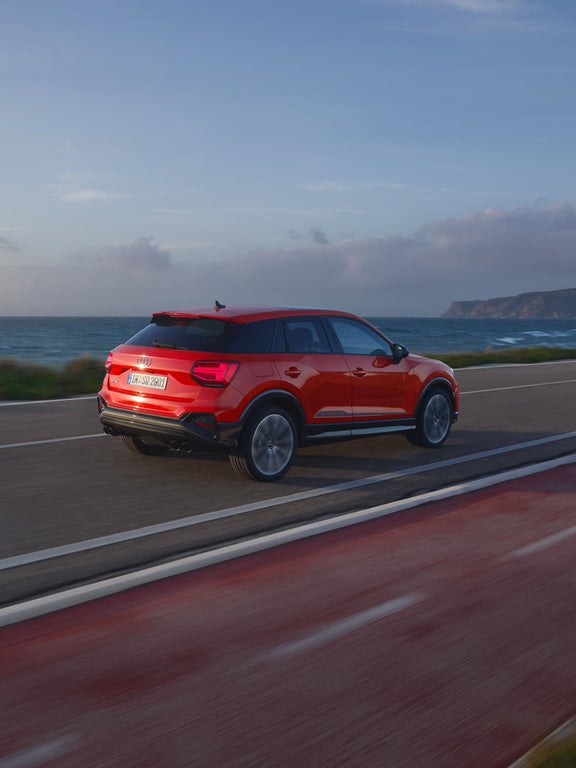 Ein roter Audi SQ2 fährt auf einer Küstenstraße am Meer entlang. Weiter hinten sieht man eine Klippe.