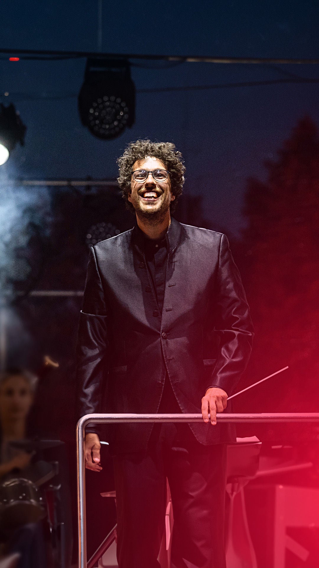 Dirgent auf Konzertbühne hinter dem Dirigentenpult im Abendlicht von Scheinwerfern angestrahlt .