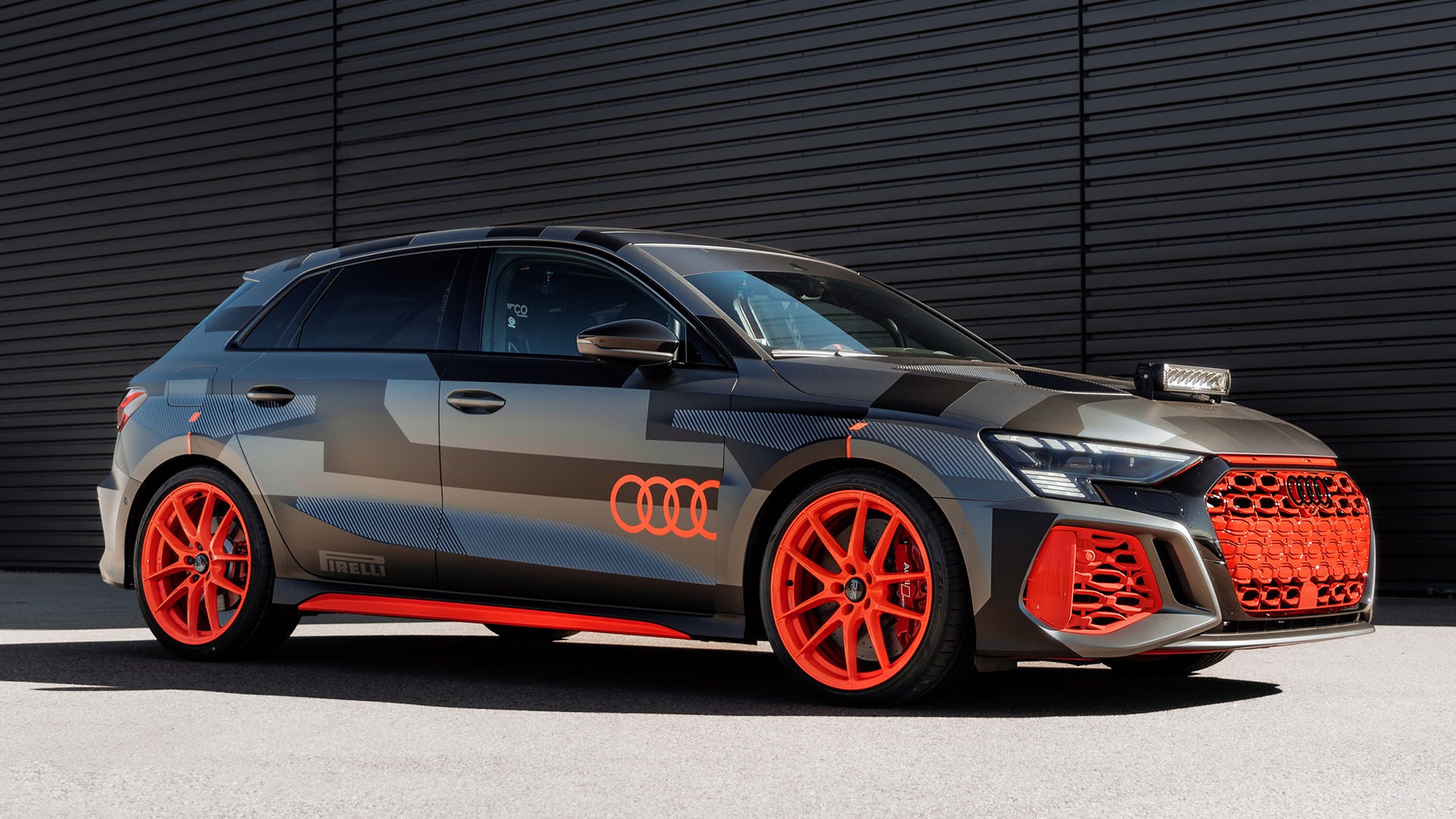 Grauer Audi RS 3 driving experience mit roter Folierung und roten Felgen steht vor schwarzer Industriehalle.