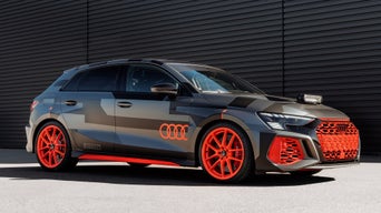 Gray Audi RS 3 driving experience with red foiling and red rims stands in front of a black industrial hall.