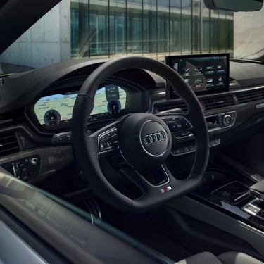 Interior view of an Audi car showing steering wheel and digital dashboard displays.