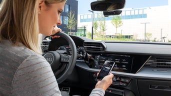 Frau sitzt im Auto und schaut auf ihr Handy