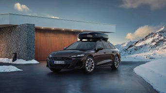 Audi mit Dachbox steht in einer Schneelandschaft vor einem Haus