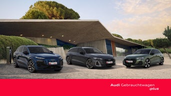 Zwei graue Audi Avant stehen versetzt auf einer weitläufigen Steinplaza vor einem großen, weißen Kubusgebäude.