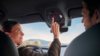 Finger berührt SOS-Taste, im Dachmodul eines Audi, die mit rotem Symbol und grüner LED-Anzeige beleuchtet ist.