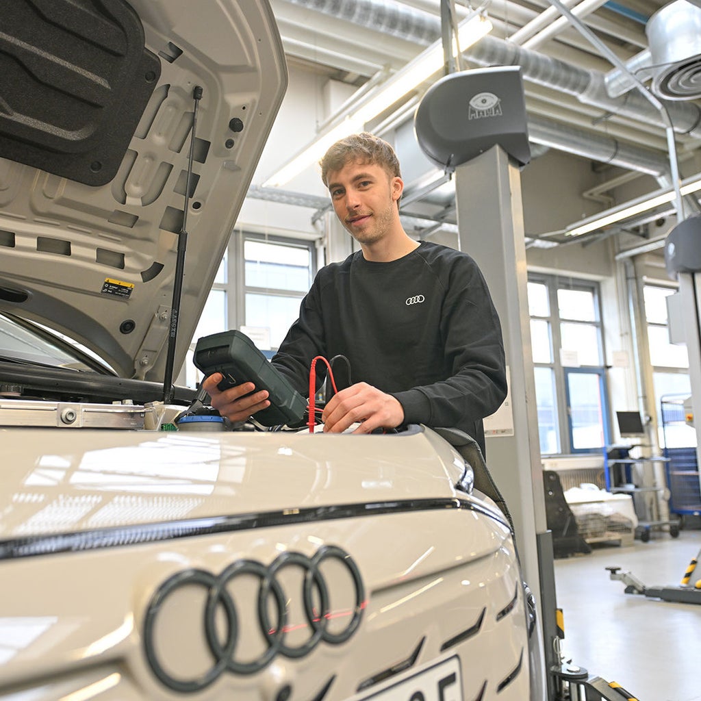 Julian steht am Motor eines Audi und hält ein Gerät in der Hand
