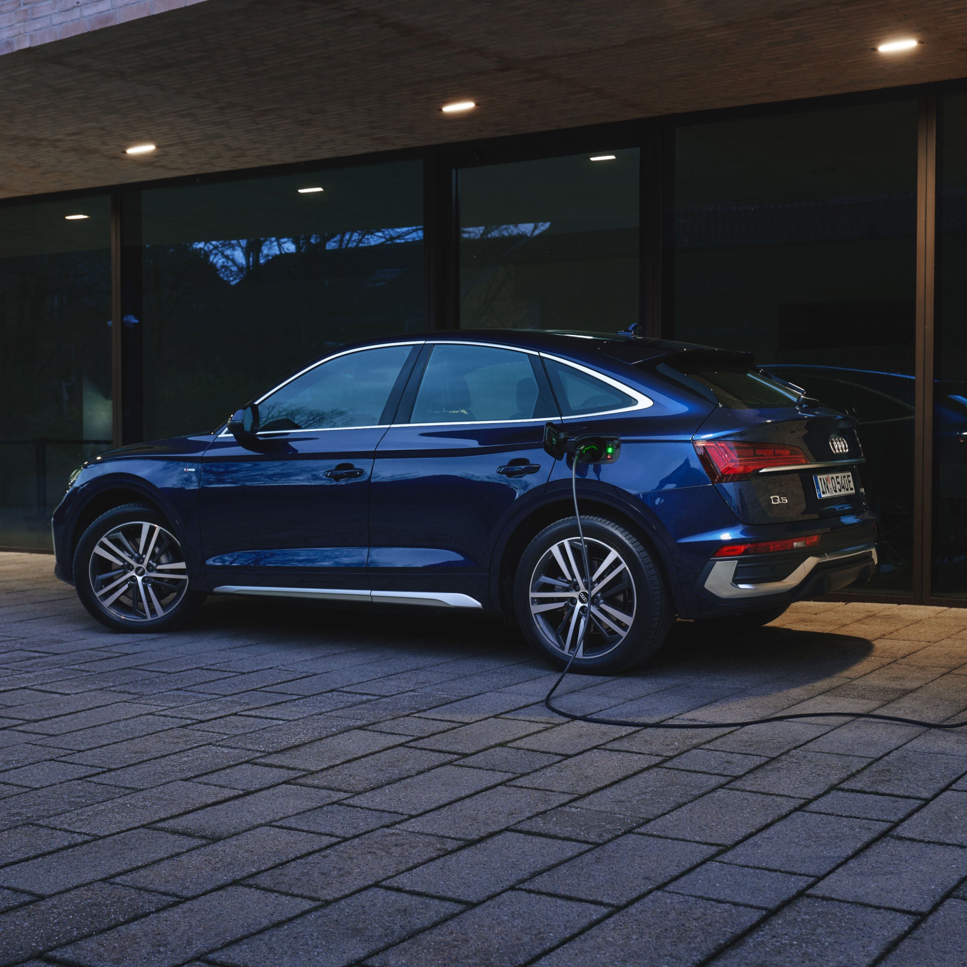 A blue electric SUV charging at a station during dusk.