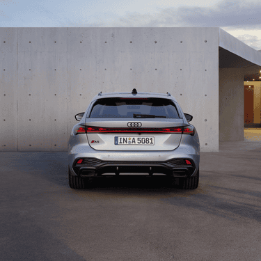 A silver Audi A5 Avant parked in front of a concrete wall with clear skies above.