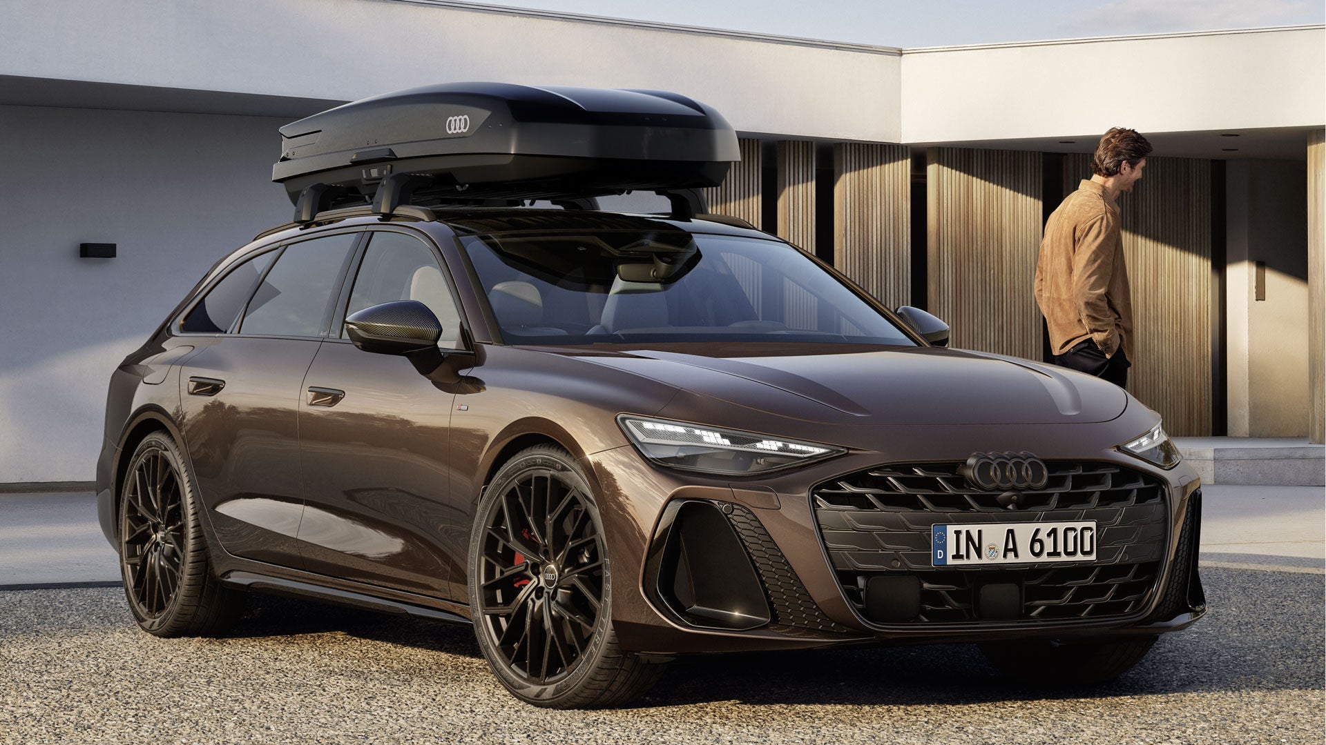 A6 Avant står i en vinkel på en grusyta framför ett modernt hus. På taket finns en takbox med Audi-logotypen.