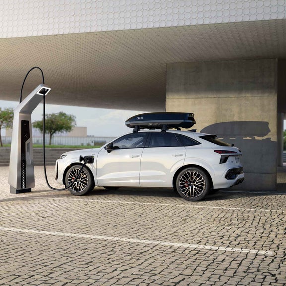 Audi Q3 SUV Sportback külgvaates parklas laadimise ajal. Valgel autol on näha ka katuseboks.