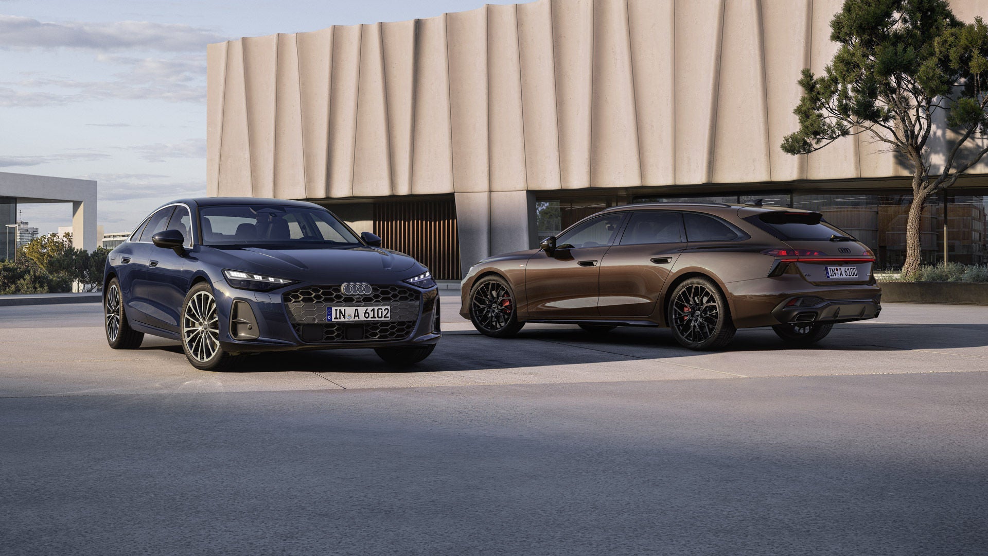 Dos vehículos eléctricos de Audi frente a un edificio moderno al atardecer en una superficie de concreto abierta.