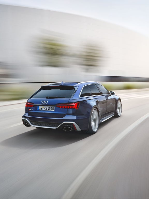 Dunkelblauer Audi RS 6 Avant fährt auf leerer Straße, das Fahrzeug ist von hinten schräg links zu sehen.