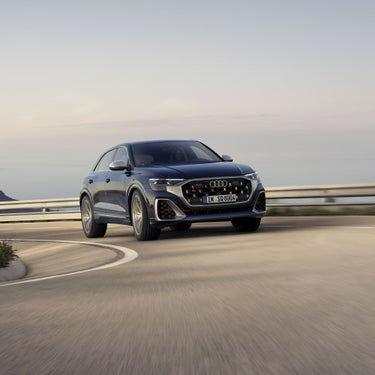 Ein dunkelblauer Audi SQ8 SUV fährt auf kurviger Straße mit leichter Neigung.