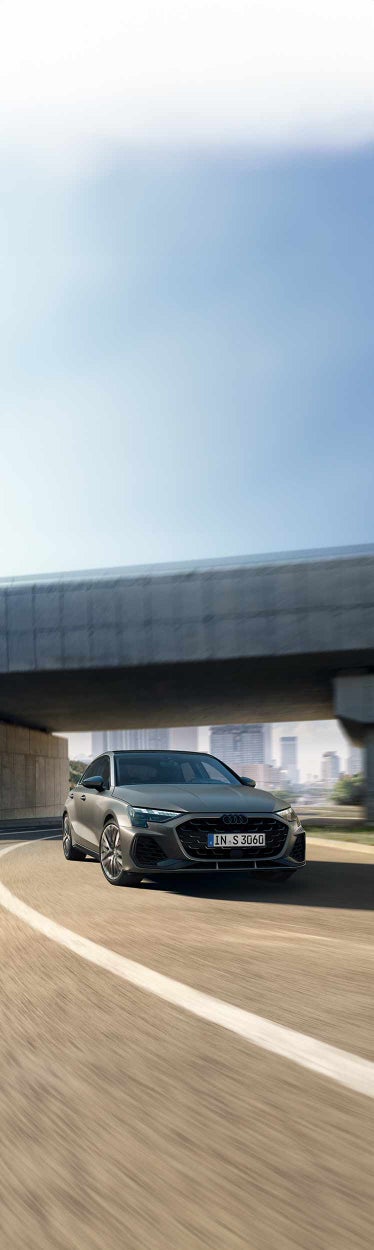Frontansicht eines silbernen Audi S3 Sportback in Fahrt auf einer Stadtstraße bei Tageslicht.