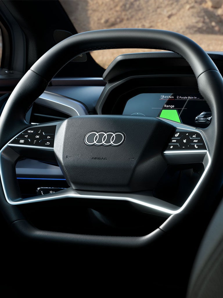 Blick auf das Cockpit eines Audi Q4 Sportback e‐tron mit kantigem Lenkrad, Touch-Bedienelementen und digitalem Tacho im Hintergrund.