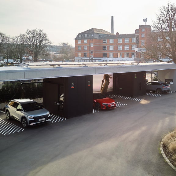 Drei Audi Elektrofahrzeuge laden an überdachten Ladesäulen neben dem Gebäude „Klassikstadt“.