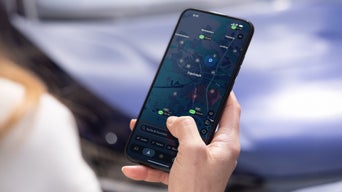 Person hält Smartphone mit Karten-App vor einem Fahrzeugdisplay mit Audi-Menüanzeigen.