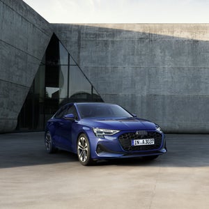 Een blauwe A3 Limousine staat geparkeerd voor een modern gebouw.