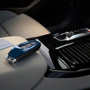 A car key fob rests on a light grey leather car seat next to a shiny black console, conveying modern luxury and elegance.