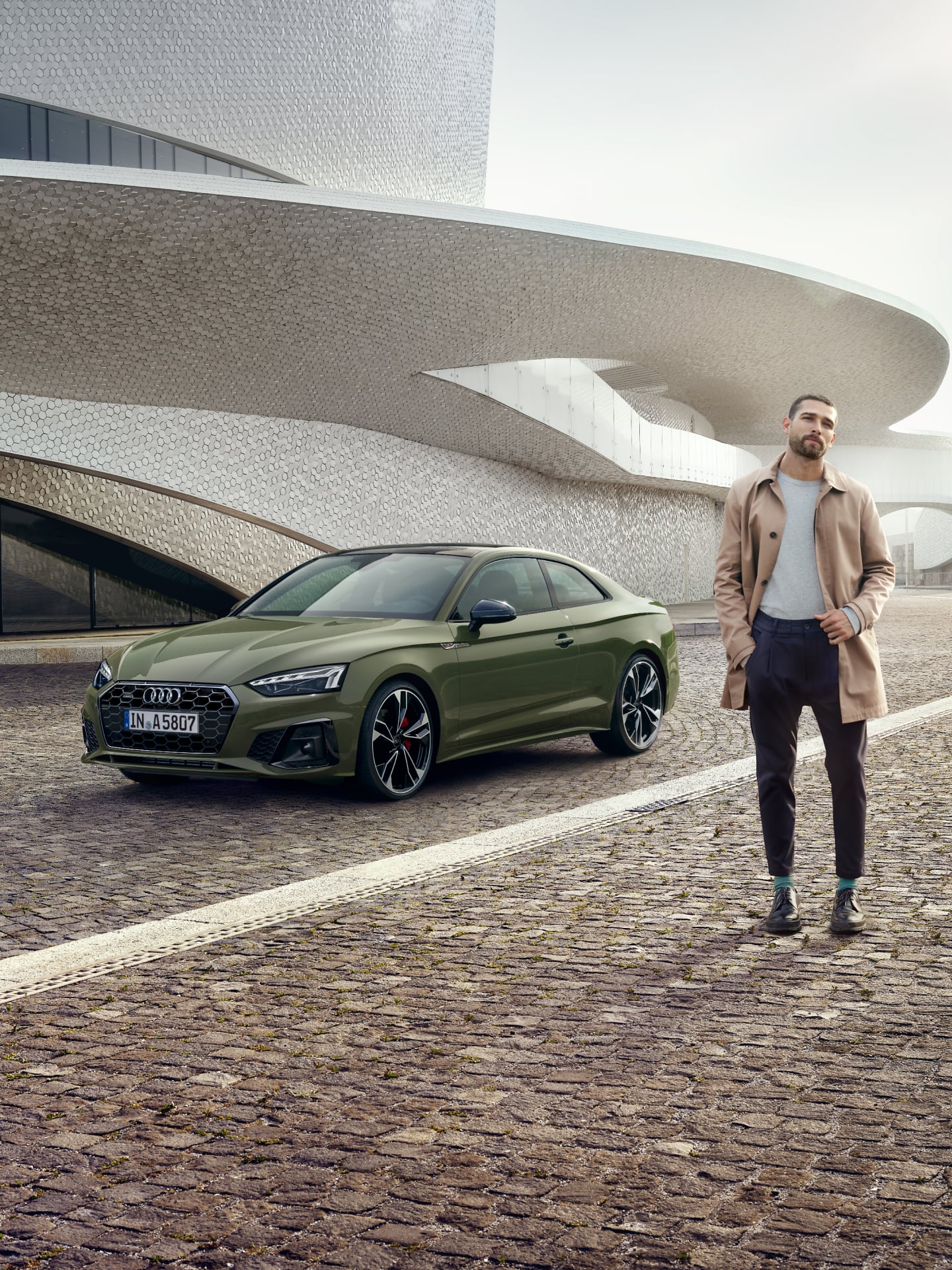 A green Audi car parked beside a modern building with a person standing nearby.