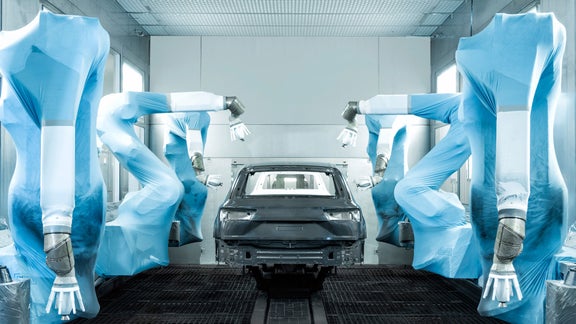 Lackierroboter in blauen Schutzüberzügen sprühen Farbe auf eine schwarze Karosserie in einer Lackierstraße.