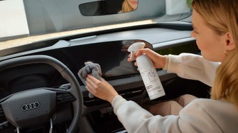 Eine Frau putzt mit dem Universal-Reinigungstuch von Audi die Armatur eines Audis