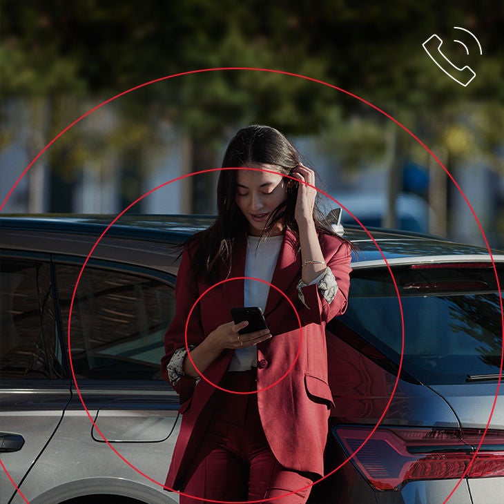 Eine Frau lehnt an einem Auto und bedient ein Smartphone