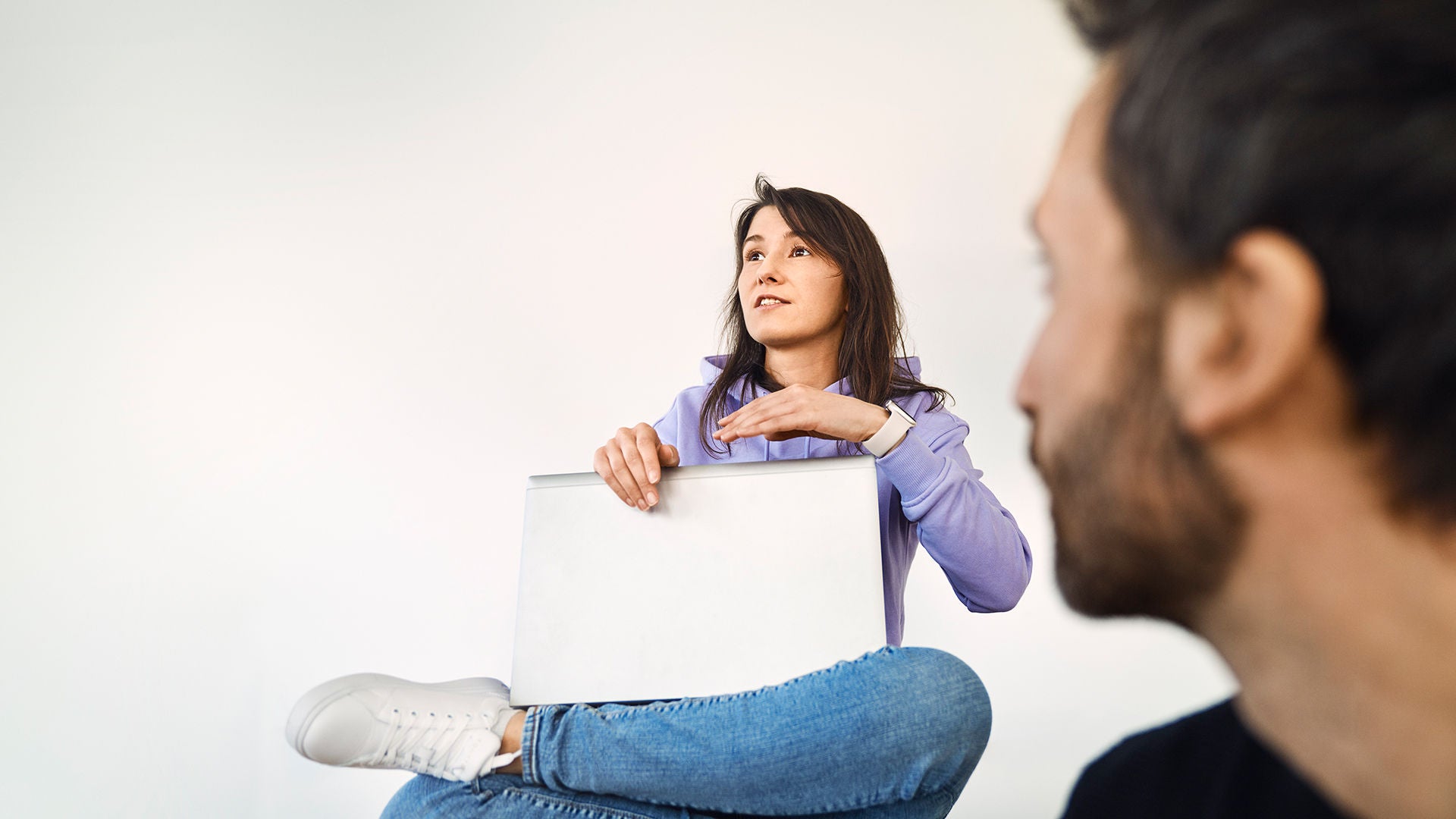 Sevgi sitzt mit ihrem Laptop auf dem Schoß und sagt etwas. Ein Kollege sitzt vor ihr