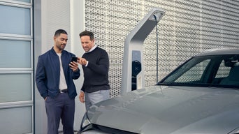 Zwei Männer vor einer Ladestation schauen gemeinsam auf ein Smartphone neben einem Audi.