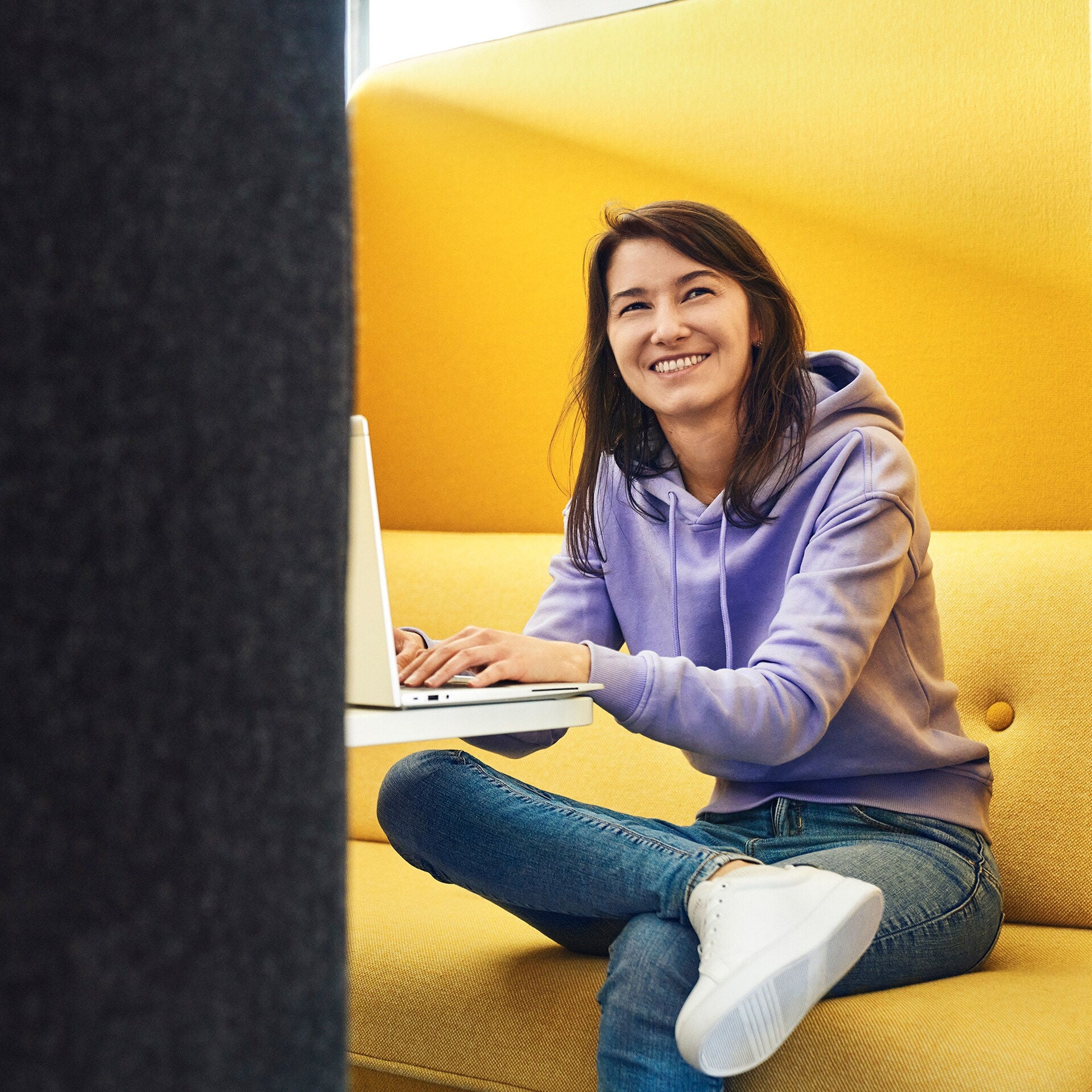 A woman laughs into the camera and types on a laptop
