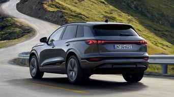 Schräge Heckansicht des SQ6 SUV e-tron, welcher durch kurvige Straßen in einer bergigen Landschaft fährt.