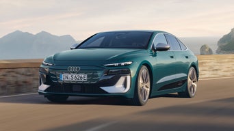 A sleek teal Audi S6 Sportback e-tron drives along a coastal road with mountains in the background.
