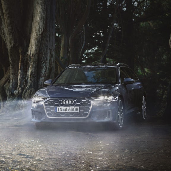 Audi car driving on a forest road with light mist around it.
