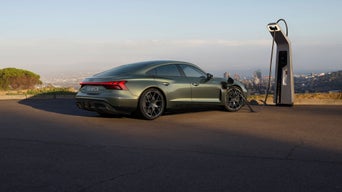 A green electric car parked and charging at a modern station, overlooking a cityscape under a clear sky.