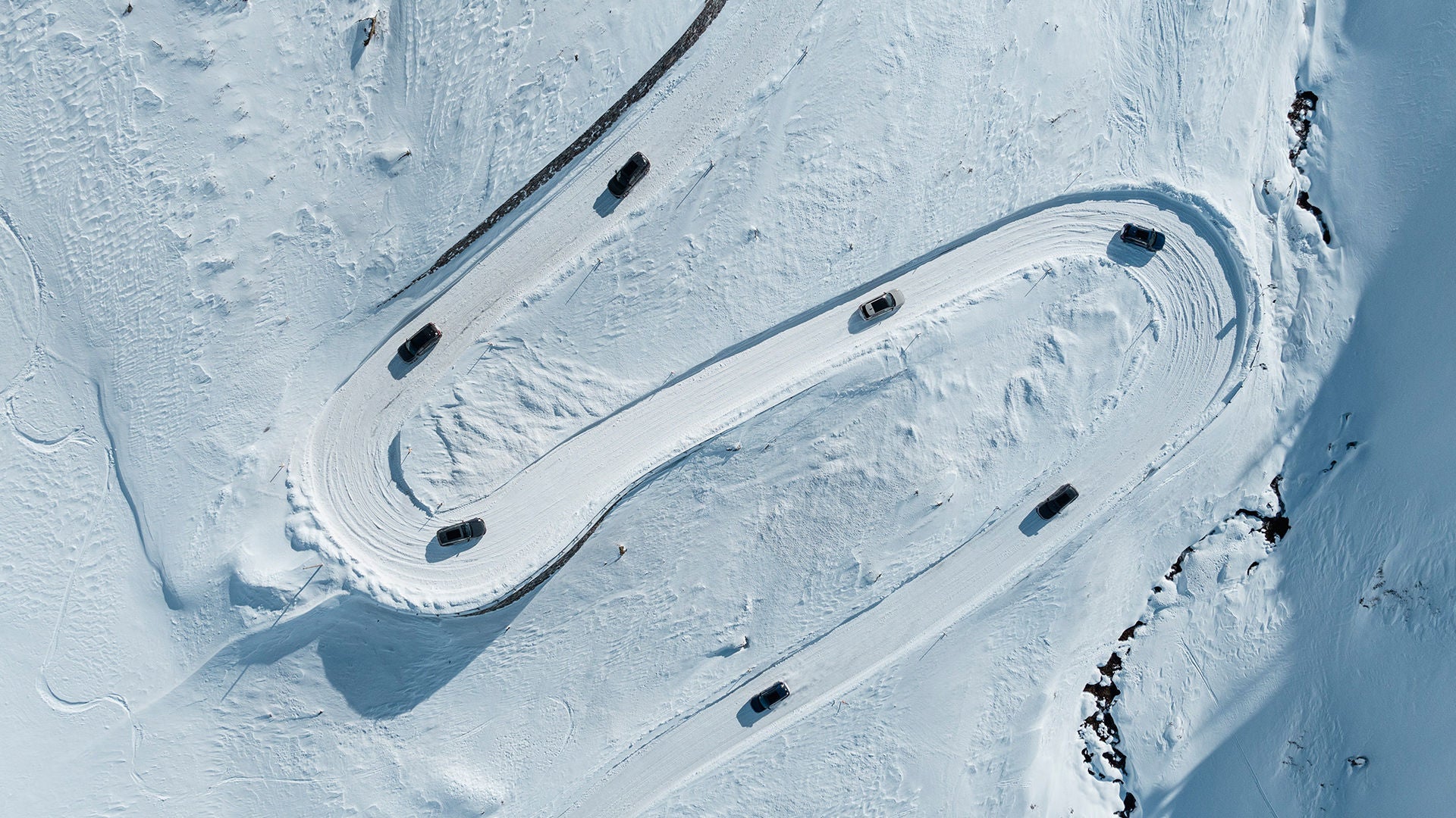 Several cars driving on a snowy winding road, photographed from a bird's eye view.
