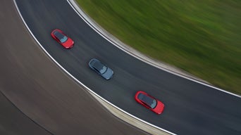 Draufsicht auf drei Audi Fahrzeuge, zwei rot und eines grau, auf einer Rennstrecke in einer Linkskurve.