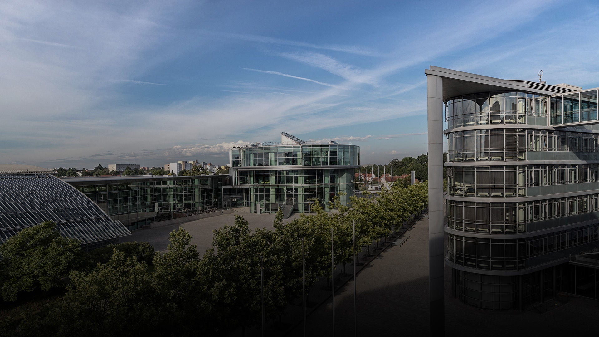 View of modern buildings with glass facades, wide forecourt and green area in daylight.