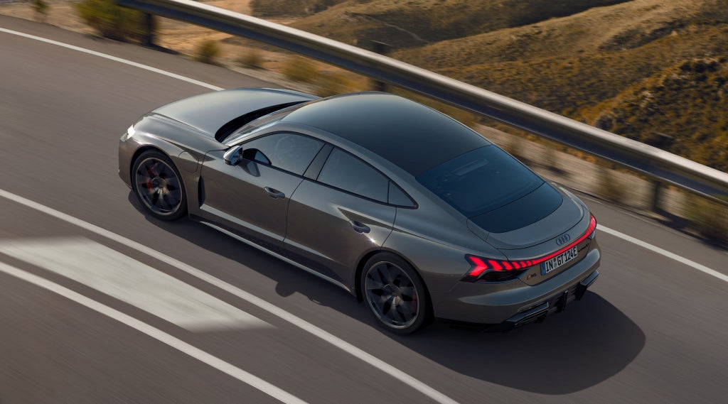 Ein grauer Audi RS e-tron GT fährt auf einer kurvigen Bergstraße mit leuchtenden Rücklichtern.