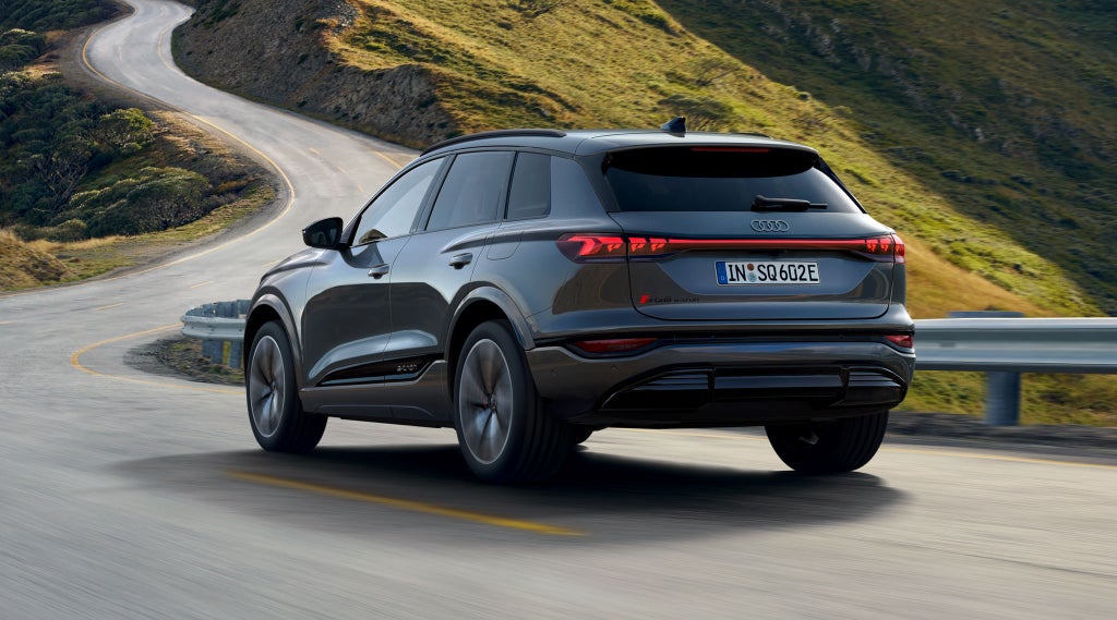 Schräge Heckansicht des SQ6 SUV e-tron, welcher durch kurvige Straßen in einer bergigen Landschaft fährt.