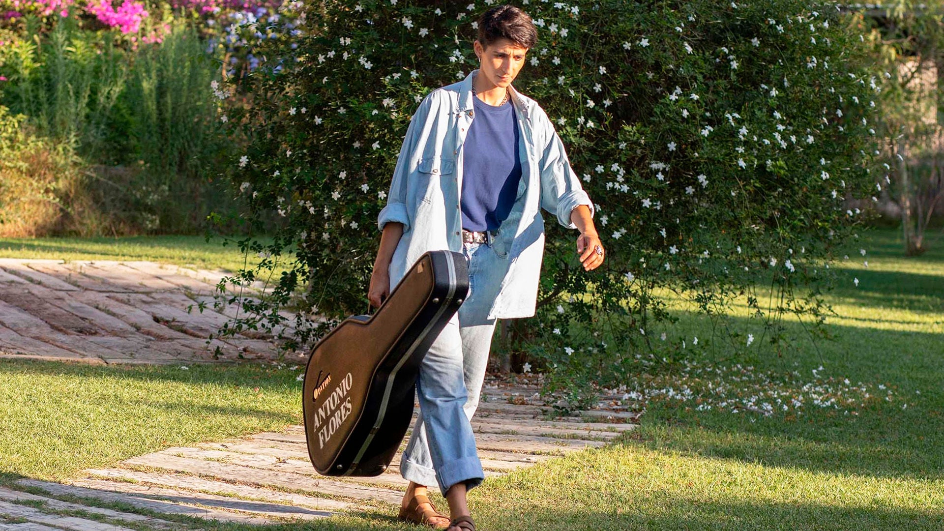 Eine Frau geht mit einem großen Gitarrenkoffer durch einen Park.