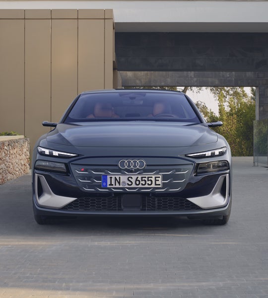 Frontprofil des S6 Avant e-tron, welcher auf Pflastersteinen vor einem modernen Gebäude steht.