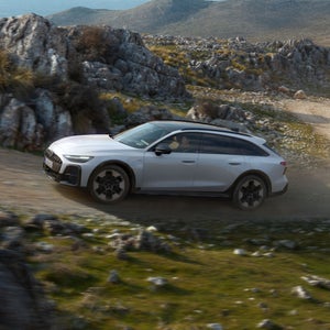 Audi A6 allroad e-hybrid kör längs en brant grusväg i ett klippigt landskap.