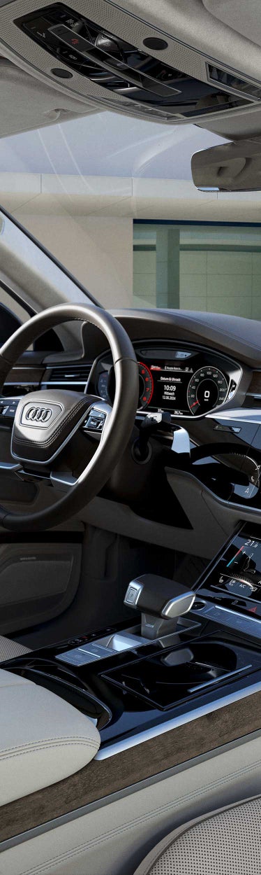 Innenraum eines Audi A8 mit digitalem Cockpit, Touchscreen und hellen Ledersitzen.