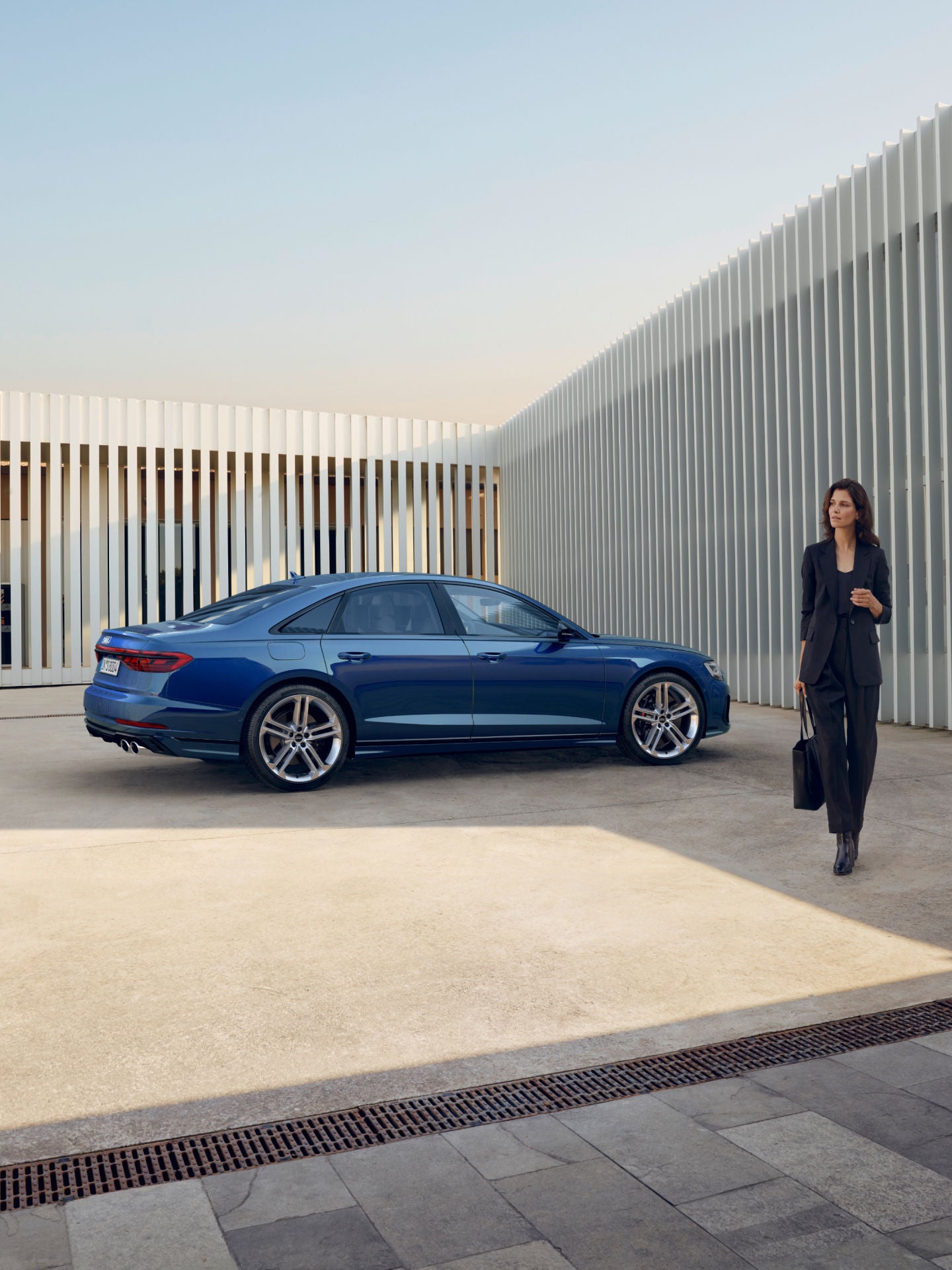 landscape image lady standing left of blue Audi A8 S8