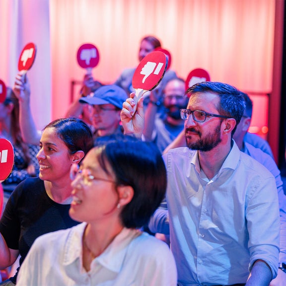 Publikum zeigt rote und schwarze Abstimmkarten mit Daumen hoch oder runter bei einer Veranstaltung.