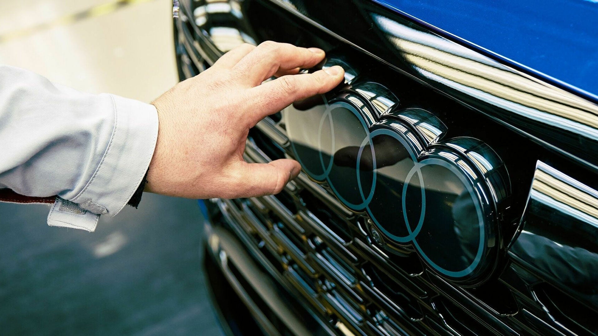 A hand touches the Audi logo on the front of a vehicle